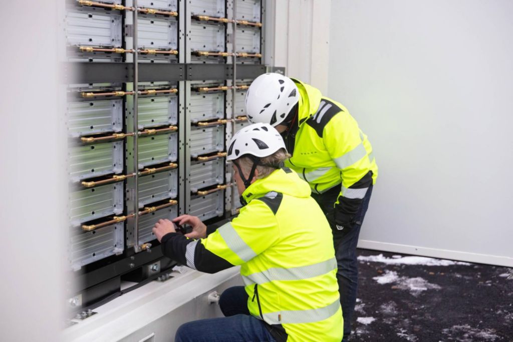2 men in hard hats at work in front of a battery