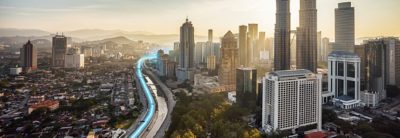 An aerial view of a Malaysian cityscape with a blue line tracing the route of an electric bus