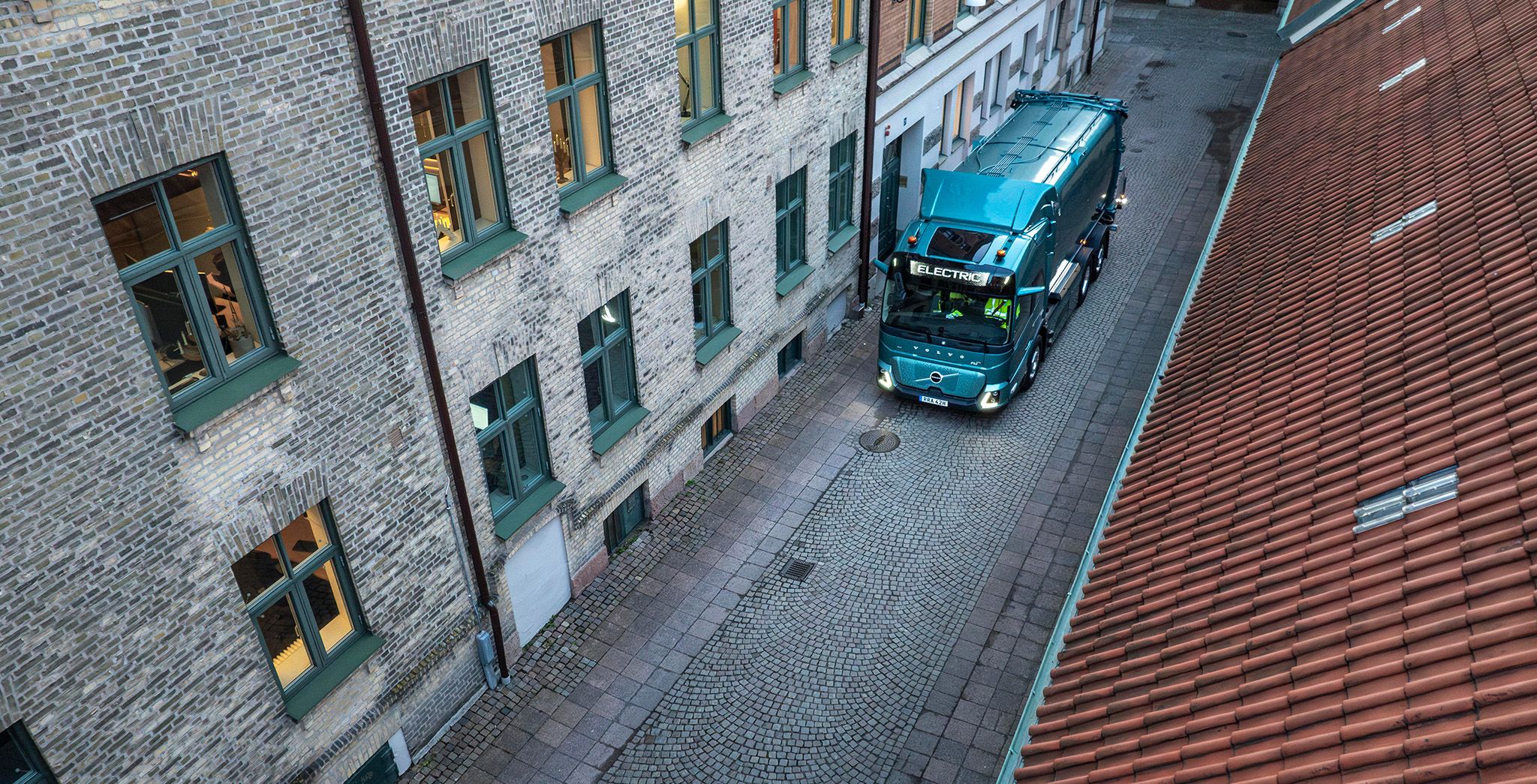 Egy kék teherautó egy keskeny, macskaköves utcában, felülről, ferdén készített fotó