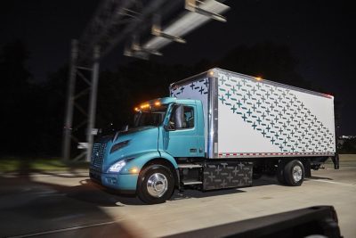 Blue Volvo VNR Electric truck with trailer attached, driving through a dark street