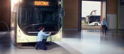 A depot technician connects a Volvo electric bus to a charging station.