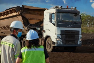 A large white Volvo semi-truck is operating at a worksite with dirt and heavy equipment around it.
