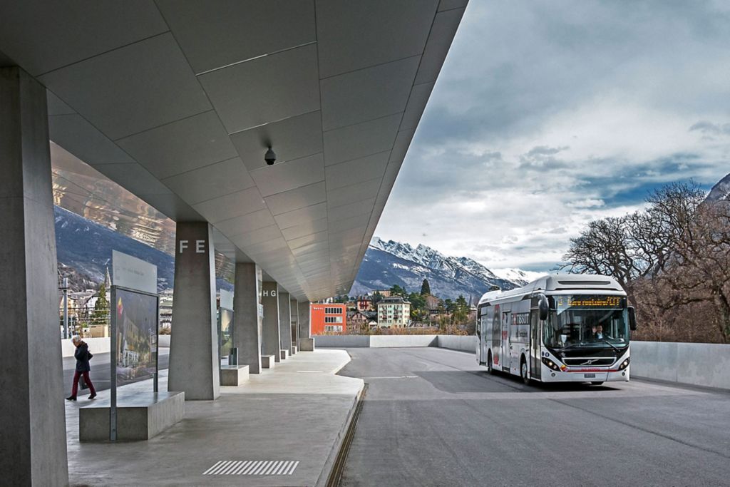 A Volvo full hybrid bus in Sierre's modern bus station with mountains in the background