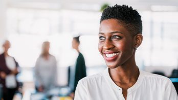 A woman is standing at the forefront with a big smile on her face, in the blurry background you can see three people.