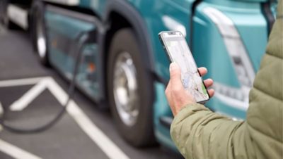 A man holding a phone, standing next to a charging electric truck.