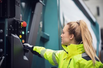 A driver in a high-visibility jacket operates the side controls of a Volvo truck, illustrating skilled, well-trained drivers who keep operations safe, efficient, and productive.