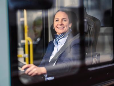 Female bus driver looking out through the side window, smiling.