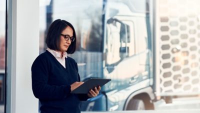 A woman stands in front of a Volvo truck looking at a tablet