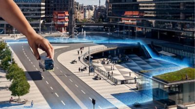 A giant hand places a Volvo bus onto a city street.