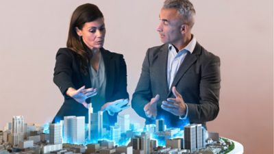Two persons in a discussion over a model of a city, illuminated by a blue light.