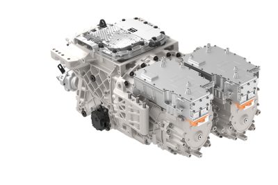 Zeer gedetailleerde studiofoto van een elektrische aandrijfeenheid met dubbele elektromotorbehuizingen met oranje hoogspanningsconnectoren, geïntegreerde vermogenselektronicamodules en een centrale versnellingsbakstructuur. De assemblage wordt getoond tegen een effen, lichte achtergrond om de componenten en bevestigingspunten te benadrukken.