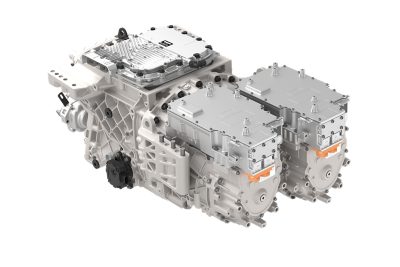 High‑detail studio image of an electric driveline unit featuring dual electric motor housings with orange high‑voltage connectors, integrated power electronics modules, and a central gearbox structure. The assembly is shown against a plain light background to highlight components and mounting points.