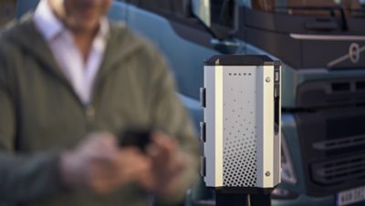 Close-up of an electric vehicle charger with a blurred person using a phone near a truck in the background.