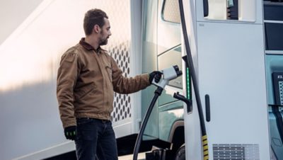 A man standing next to an electric truck inserting the charging cable from a Volvo Energy charging station.