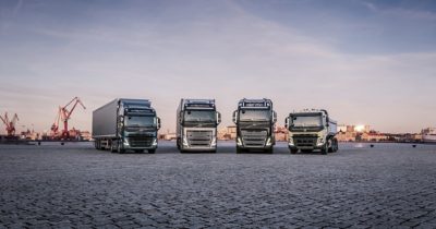Four trucks stand in a row in front of a crane