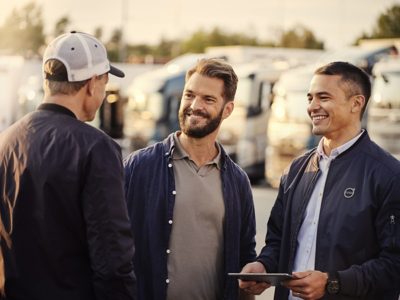 Tre mænd i samtale foran en flåde af lastbiler