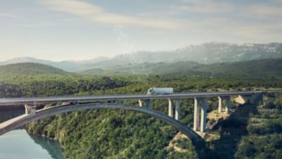 A truck drives over a bridge with water and trees below