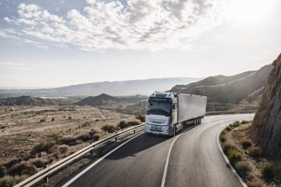 A Volvo Truck drives on a bridge over water as the sun sets behind it