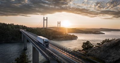 Nákladné vozidlo Volvo jazdí po moste nad vodou, keď za ním zapadá slnko