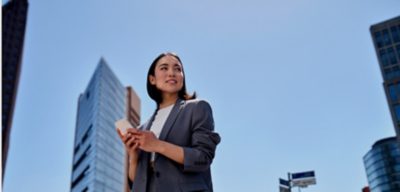 Young busy successful beautiful Asian business woman, korean professional businesswoman holding cellphone using smartphone standing or walking on big city urban street outside.