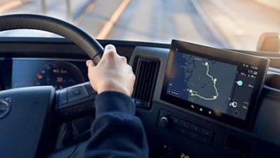 Close up image of a persons hand driving a truck with a digital map to the right