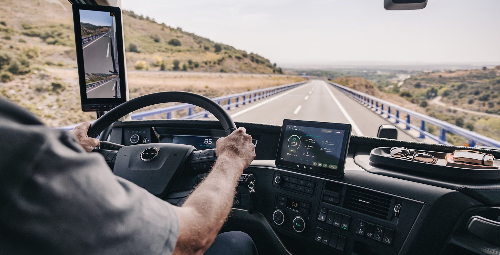 Iz unutrašnjosti kabine kamiona Volvo, s obje ruke na upravljaču, vozač upotrebljava sustav nadzora s kamerama