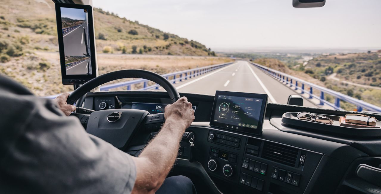 A Volvo teherautó fülkéjéből, mindkét kéz a kormánykeréken, kamerás monitorrendszer használatban