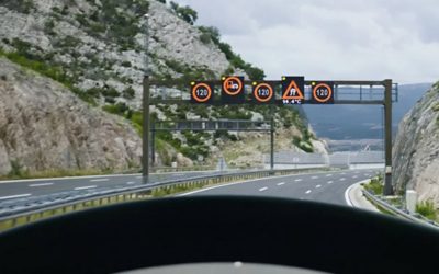 Camion care circulă pe o șosea înconjurată de munți și prevăzută cu indicatoare rutiere 