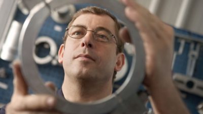 Imagem aproximada de um homem inspecionando uma peça de reposição Volvo, examinando a qualidade premium e atenção aos detalhes.