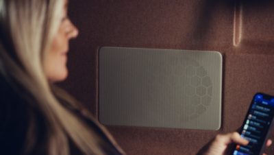 Une femme blonde assise à côté d'un haut-parleur tenant un téléphone portable et le regardant