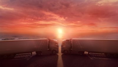 Two Volvo FH with I-Save trucks face each other with cabs almost touching as the sun sets behind them
