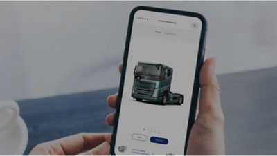 A hand holds a mobile phone displaying the Volvo Truck Builder tool
