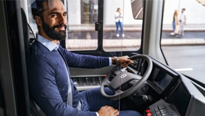 A smiling bus driver behind the steering wheel of a Volvo electric bus