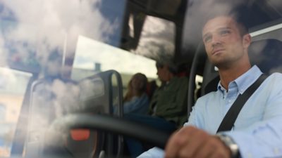 A male coach driver behind the steering wheel, looking ahead through the windscreen 