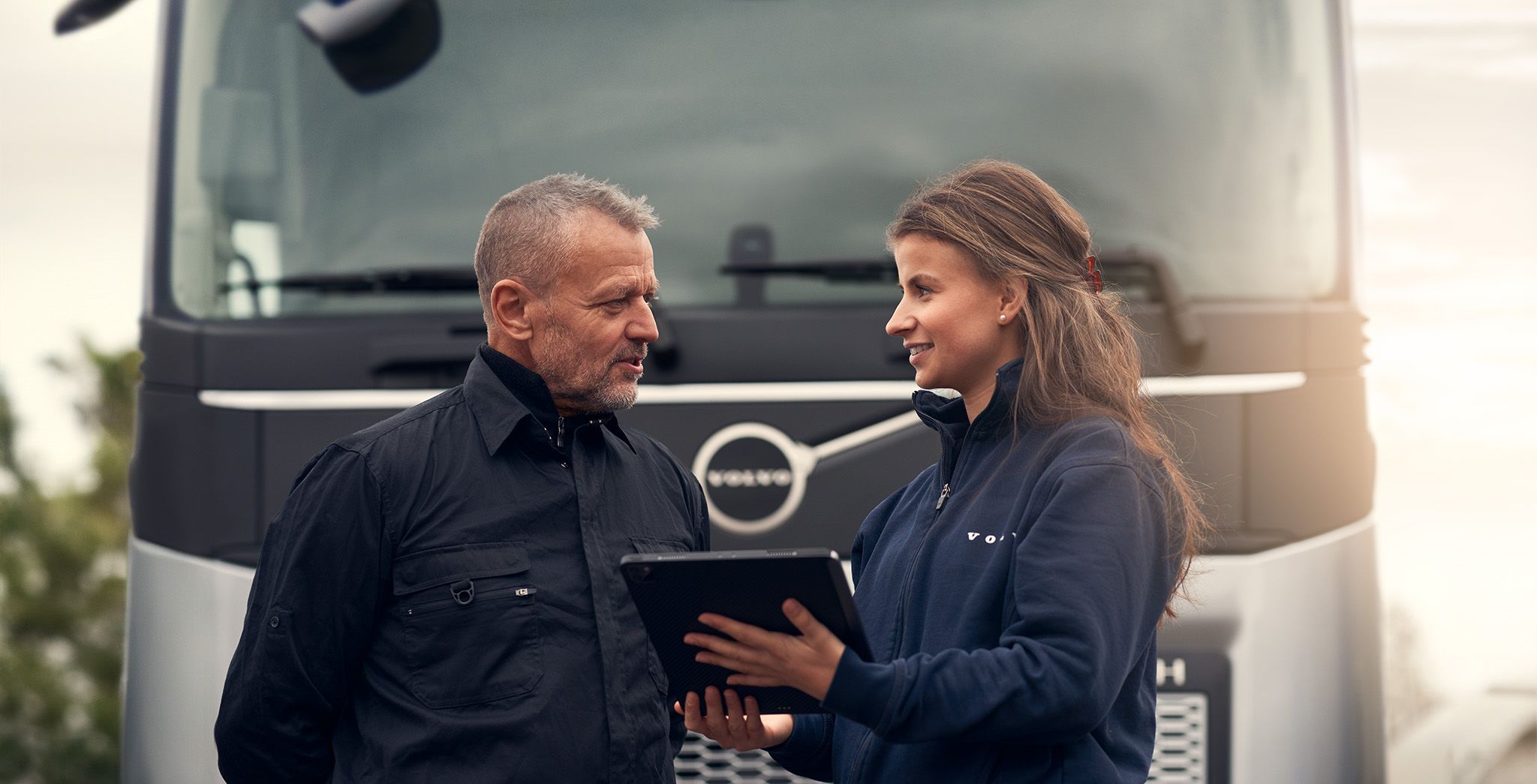 Man och kvinna pratar framför en lastbil och håller i en digital skärm