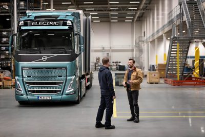 Mekaniker og lastbilschauffør taler sammen i lagerbygning foran Volvo FH Electric