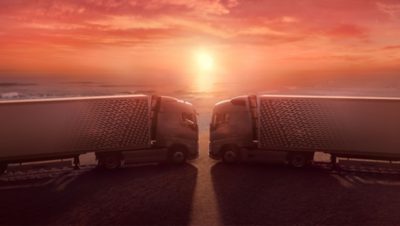 Deux véhicules Volvo FH avec I-Save sont face à face, les cabines se touchent presque et le soleil se couche derrière eux