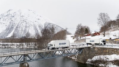 To-av-Veøys-Volvoer-kjører-over-bru-i-vakre-omgivelser. 
