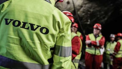 A work team is standing in a mine, all dressed in red overalls with Volvo vests over them and helmets.
