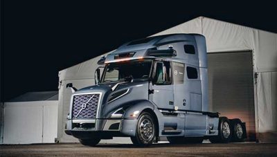  Autonomous Volvo semi-truck with the Aurora driver standing in front of a warehouse.