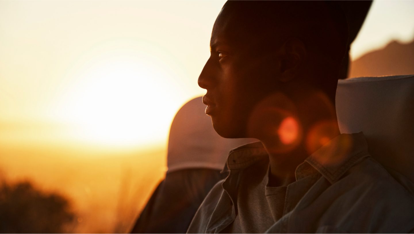 A male passenger looking at a sunset through the window of a bus