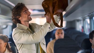 Male passenger loading a bag on the overhead shelf of a Volvo bus