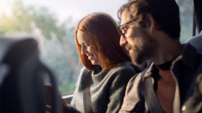 A couple sitting next to each other in a coach, looking at a tablet or a magazine