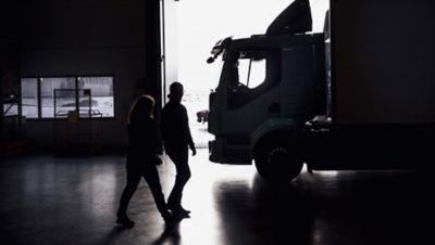 Two people walking past a truck in a dimly lit warehouse.