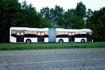 An articulated full hybrid bus drives alongside crops in a field