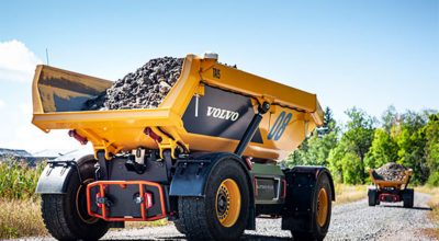 Two Volvo TA15 electric dumpers filled with crushed stone are driving on a road
