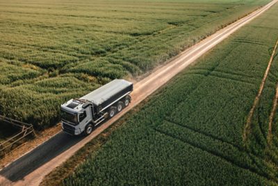 Duża ciężarówka jadąca po nieutwardzonej drodze otoczonej zielonymi polami.