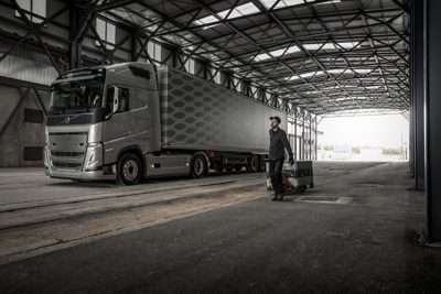 Muž s ručným nákladným vozíkom kráča okolo nákladného auta vo vnútri nakladacej rampy