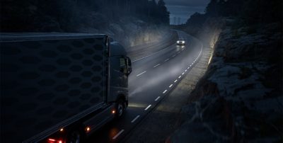 Self driving Volvo truck driving on a road at night, meeting a Volvo car in the opposite car lane.