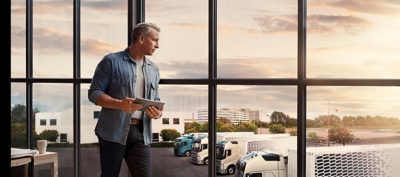 Företagsägare ser över sin Volvo-lastbilsvagnpark på gården och planerar rutter med hjälp av Volvos lastbilstjänster.